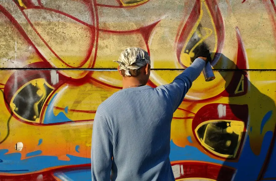A person spray-painting graffiti on a wall.